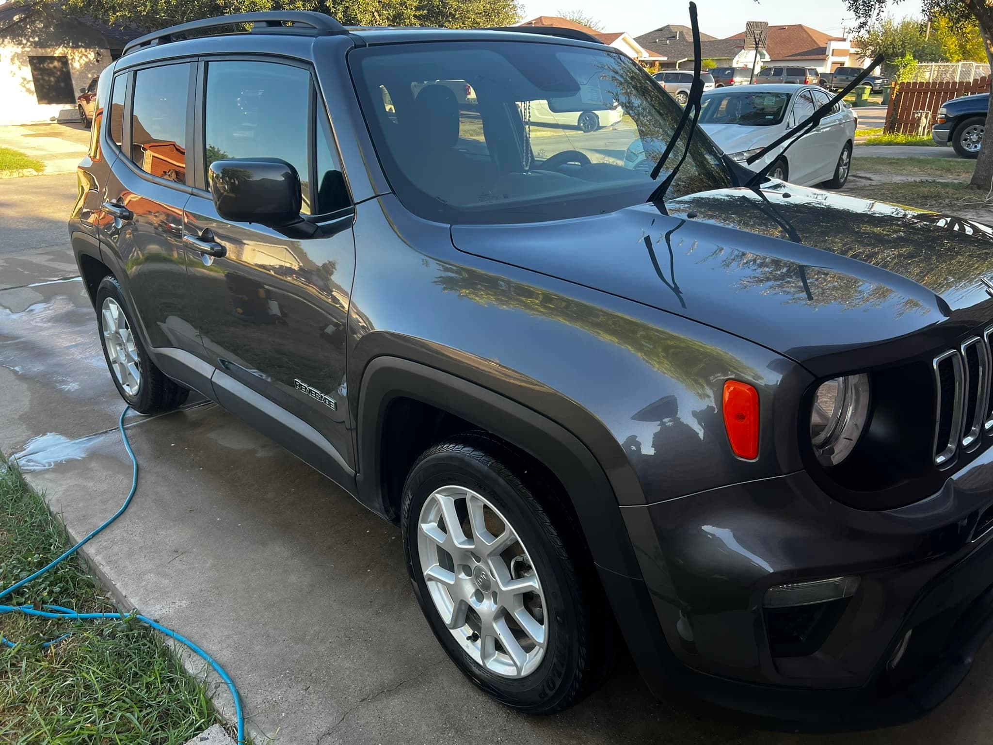 Graphite Jeep Renegade mid-wash, suds still running off the driveway
